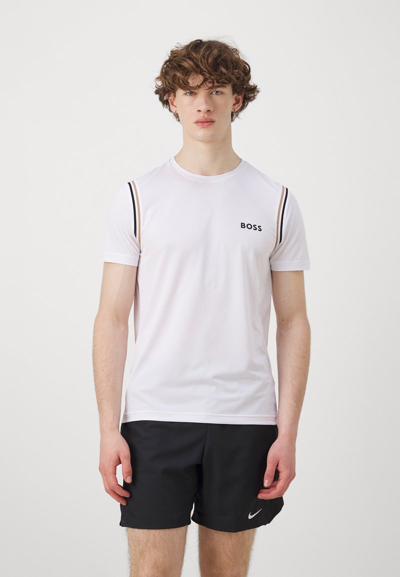 Camiseta atlética de manga corta blanca con el logo negro "BOSS", que presenta rayas horizontales tonales en las mangas, combinada con pantalones cortos negros.