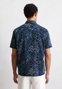 Korte mouwen overhemd van marineblauwe stof met een bloemenpatroon in lichtblauw en wit. Standaard kraag met een rechte snit en zijslits.