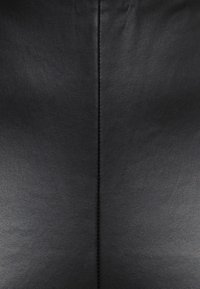 Svart läder med en slät yta, featuring en central söm. Ytan uppvisar en subtil glans som framhäver dess eleganta design.