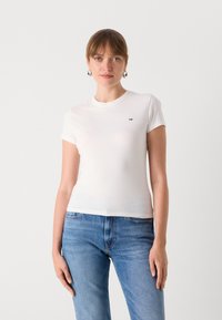 T-shirt en coton blanc à manches courtes, design ajusté, avec un petit logo multicolore sur la poitrine gauche. Associé à un jean en denim bleu.
