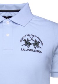 Camisa polo azul claro hecha de tela texturizada. Presenta una tapeta de tres botones y un logotipo bordado con dos jugadores de polo y mallets cruzados.