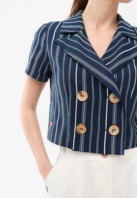 Granatowa, krótka marynarka o krótkim rękawie, z białymi paskami, podwójnymi guzikami, detalami z drewnianych guzików i kołnierzem z wycięciem.