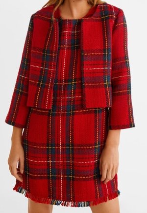Femme portant une robe à carreaux rouge avec une veste courte assortie, toutes deux ornées de franges et à manches longues.