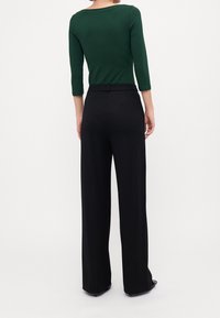 Groen nauwsluitend shirt met driekwartmouwen, gecombineerd met zwarte, wijde broek met hoge taille, met een gladde textuur en eenvoudige silhouet.