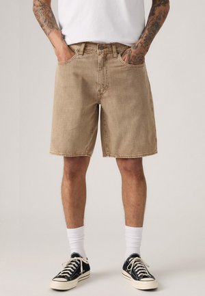 Beige denim shorts with a relaxed fit, featuring front pockets and a button closure, paired with black sneakers and white socks.