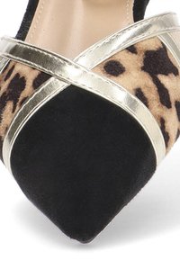 Zapatos negros de ante con punta afilada y sección media de estampado de leopardo, que cuentan con tiras cruzadas metálicas doradas. Superficie texturizada y detalles de diseño elegantes.