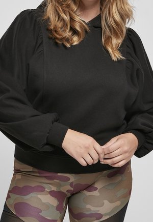 Sweatshirt noir à manches bouffantes, poignets côtelés et capuche. Associé à des leggings à motif camouflage aux tons terreux.
