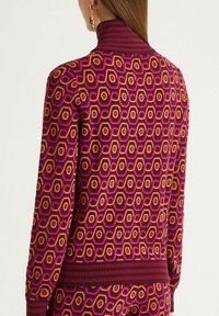 Pull en maille avec un motif hexagonal rose et orange, doté d'un col montant côtelé et d'un ourlet côtelé pour plus de texture.