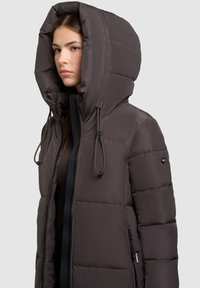 Ciemnobrązowa kurtka puchowa z dużym kapturem, posiadająca zamek z przodu, regulowane sznurki i poziomy wzór przeszyć.