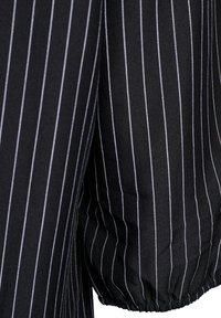 Pogled od blizu na črn tkanino z belimi črtami, ki prikazuje gubano in elastično zapestje.