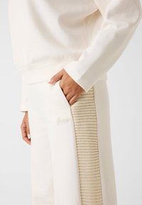 Felpa crema e pantaloni, con pannelli laterali beige testurizzati e un piccolo logo ricamato. Tessuto morbido con una vestibilità rilassata.