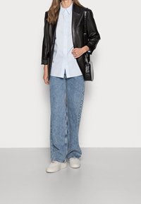 Černá kožená blejzr přes světle modrou košili s knoflíky, v kombinaci s širokými světle modrými džíny a bílými teniskami. Malá černá kabelka.