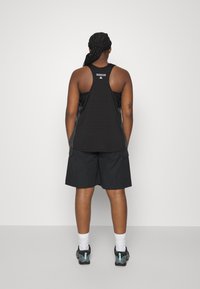 Zwarte sport tanktop met racerback ontwerp, gecombineerd met zwarte shorts. Kenmerken zijn functionele zakken en lichtgewicht, ademend materiaal.