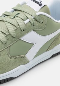 Zelené semišové a syntetické tenisky s bílými koženými akcenty, kulatými tkaničkami a texturovanou černou gumovou podrážkou.