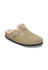 Zuecos de ante beige con un interior peludo, correa ajustable con hebilla plateada y suela de goma negra con un diseño texturizado.