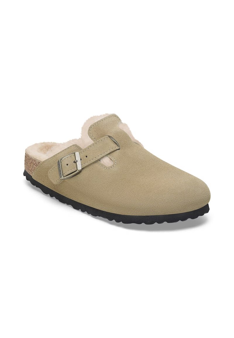 Sabots en daim beige avec un intérieur moelleux, une sangle en boucle argent ajustable et une semelle en caoutchouc noir avec un cramponnage texturé.