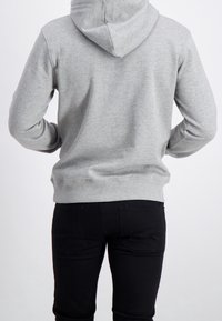 Felpa grigia con cappuccio, dalla consistenza morbida, con una vestibilità comoda e polsini a coste, abbinata a jeans neri attillati, vista da dietro.