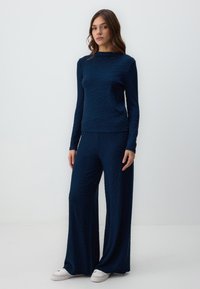 Completo navy a due pezzi con top a maniche lunghe e pantaloni a gamba larga, caratterizzato da motivi a onde testurizzati, abbinato a sneaker bianche.