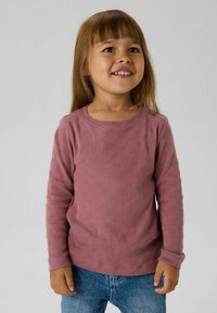 Różowa dziecięca koszula z długim rękawem o fakturowanym wzorze. Dekolt typu crew oraz dopasowane rękawy, zestawiona z niebieskimi dżinsami.