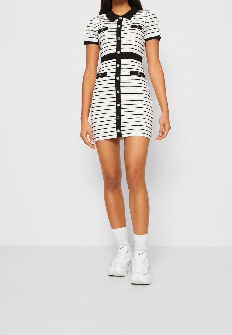 Robe courte à rayures noires et blanches avec un col, un corsage ajusté, des manches courtes et des boutons à l'avant. Comprend deux poches avant.