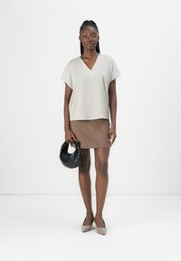 Haut gris clair à col en V avec des manches courtes, associé à une mini-jupe marron. Tient un sac à main noir, porte des escarpins beiges et gris à bouts pointus.