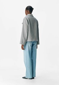 Veste en chevrons grise avec des manches larges, de coupe courte, associée à un jean large bleu clair et des chaussures noires, vue de dos.