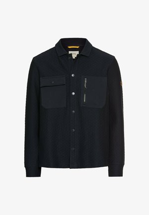 Navyblauwe shirt van geborduurde stof. Kenmerken zijn een omgevouwen kraag, twee borstzakken aan de voorkant en een ritszak aan de zijkant. Knoopsluiting.