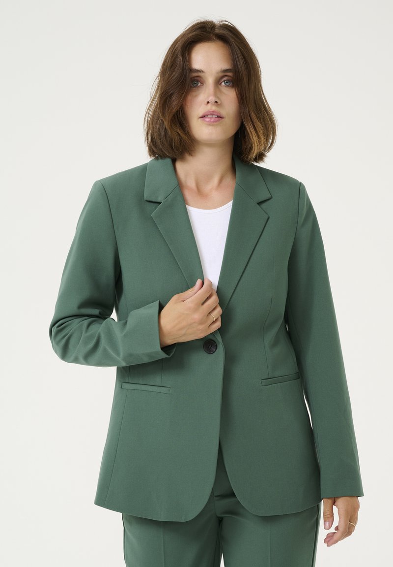 Zelený blazer vyrobený z hladké tkaniny, s klasickým klopem, zapínáním na jeden knoflík a dvěma předními kapsami, s přiléhavým střihem.