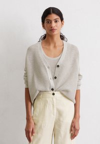 Light gray knit cardigan with a loose fit, featuring a deep V-neck, large black buttons, worn over a matching tank top and beige linen pants.