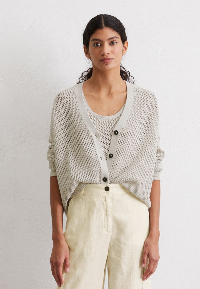 Light gray knit cardigan with a loose fit, featuring a deep V-neck, large black buttons, worn over a matching tank top and beige linen pants.