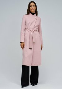 Ružičasti vuneni kaput s remenom, dužim rukavima i preklopnim ovratnikom; ima dva prednja džepa i metalni gumb kao ukras.