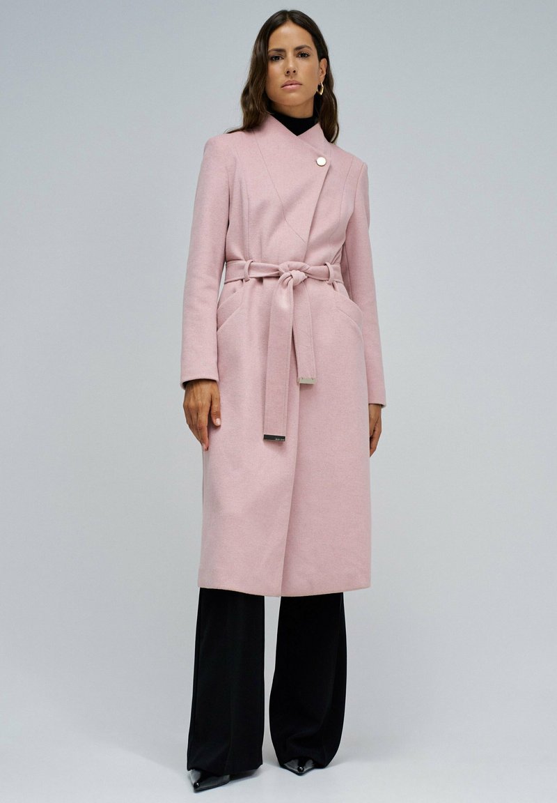 Ružičasti vuneni kaput s remenom, dužim rukavima i preklopnim ovratnikom; ima dva prednja džepa i metalni gumb kao ukras.