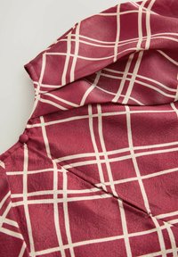 Marron stof med cremet rutenetmønster, der viser en knappet manchet og sømdetaljer på et blødt tekstureret materiale.