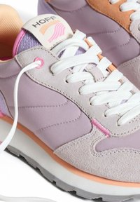 Zapatillas de color púrpura claro con materiales de ante y malla, cordones blancos, acentos rosas y una pestaña en el talón de color marrón. Presenta una suela texturizada y una etiqueta con el logotipo.