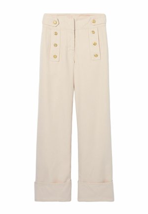 Donna in piedi rivolta in avanti, indossa un basco nero, una camicia a quadri blu, pantaloni crema a vita alta con bottoni dorati e scarpe marroni.