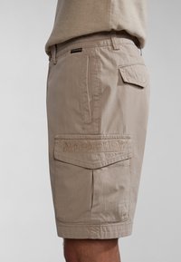 Pantalones cortos cargo beige hechos de una tela ligera, con un parche de logo bordado, bolsillos laterales y un diseño de ajuste relajado.