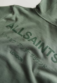 Sweat à capuche vert olive avec l'inscription "ALLSAINTS", des caractères japonais et "LONDON" imprimés en vert foncé sur le devant.