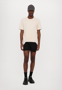 Lichtgrijze, gestructureerde, korte mouwen shirt, zwarte shorts, zwarte sokken en sneakers, met een grijze pet op het hoofd. Op zichzelf staande pose.