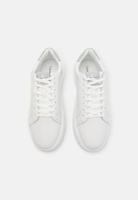 Balti ādas sporta apavi ar gludu virsmu, apaļu purngalu, šņorēšanu priekšpusē un pelēku akcentu uz papēža. Zīmols redzams uz mēles.