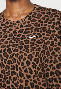 Bruine t-shirt met luipaardprint van textuurstof en subtiele ribbels; bevat een wit Nike-logo op de borst nabij de halslijn.
