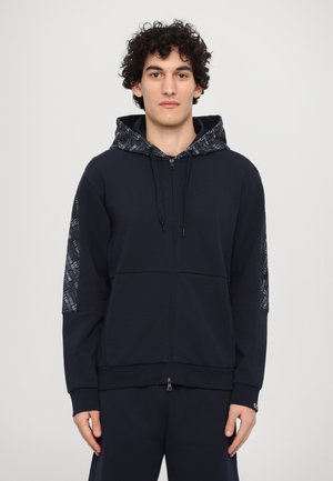 Marinblå zip-up huvtröja med en texturerad huva med mönstrad design, ribbade ärmslut och en känguruficka framtill.