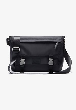 Sac messager noir en matériau durable, doté d'une fermeture à rabat avec deux boucles métalliques, d'une longue sangle réglable et d'un design élégant.
