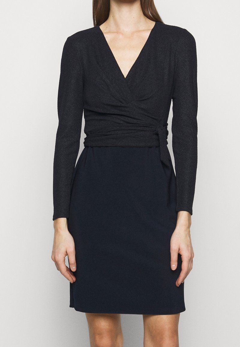 Černé šaty s výstřihem do V, dlouhými rukávy a vypasovaným korzetem se zavinovacím designem, přecházející do hladké sukně. Měkká textura.