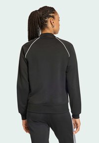 Giacca sportiva nera con design aderente, caratterizzata da rifiniture bianche lungo le spalle e i polsini, realizzata in un materiale morbido e traspirante.