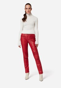 Rode leren broek met textuurdetails, gedragen met een aansluitende witte geribde coltrui. Model draagt crèmekleurige enkelboots.