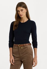 Maglione blu navy a maniche lunghe in morbido tessuto a maglia, con scollo rotondo. Abbinato a pantaloni in velluto a coste marroni e una cintura marrone con dettagli dorati.