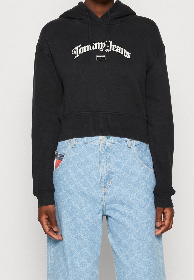 Czarny krótkoterminowy hoodie z kapturem na sznurki i białym logo "Tommy Jeans". W zestawie z jasnoniebieskimi, wzorzystymi dżinsami o luźnym kroju.