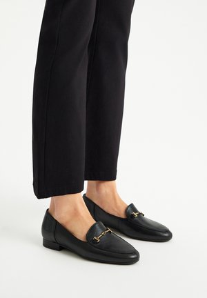 Zwarte leren loafers met een lage hak, voorzien van een decoratieve goudkleurige kettingaccent aan de voorkant en een gladde textuur. Combineer met zwarte broek.