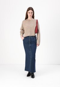 Beige und mehrfarbig gestrickter Pullover, cropped Schnitt. Dunkelblaue Jeansmaxi-Rock, gerader Schnitt, mit Seitentaschen. Rote Schultertasche und schwarze Stiefel.