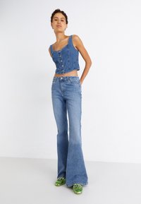 Jeans jakna s dugmadi, svjetloplave traperice širokog kroja i zelene mokasinke. Glatka tekstura, kroj po mjeri i kontrastne boje.